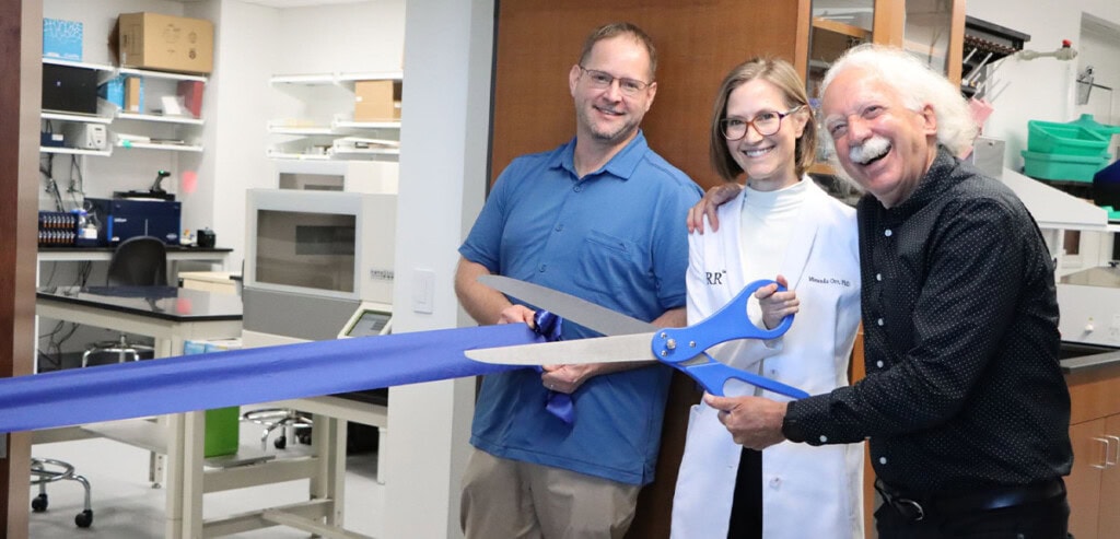 Timothy Orr, Miranda Orr, and Joe Beechem use a giant scissors to cut a ribbon into the new Orr Lab at Wash U in St. Louis.